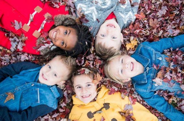 Kids in rain jackets lying in a bed of leaves - canva image Kids in rain jackets lying in a bed of leaves - canva image